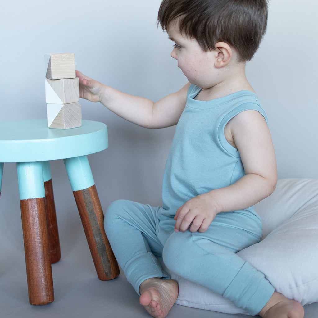 Toddler plays with wood blocks while wearing a cute romper