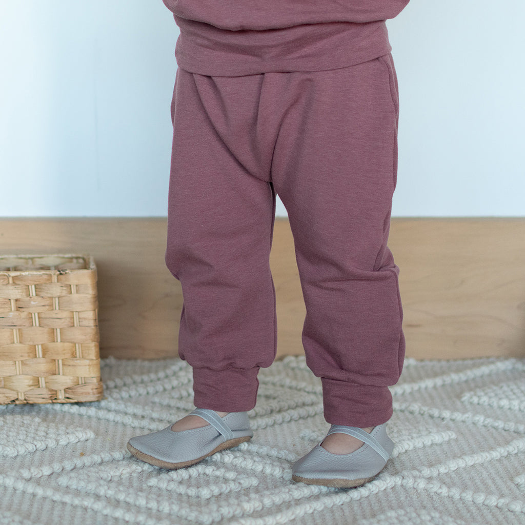 A toddler standing up, wearing harem pants in grow-with-me sizing. The colour is a warm berry tone with purple undertones.