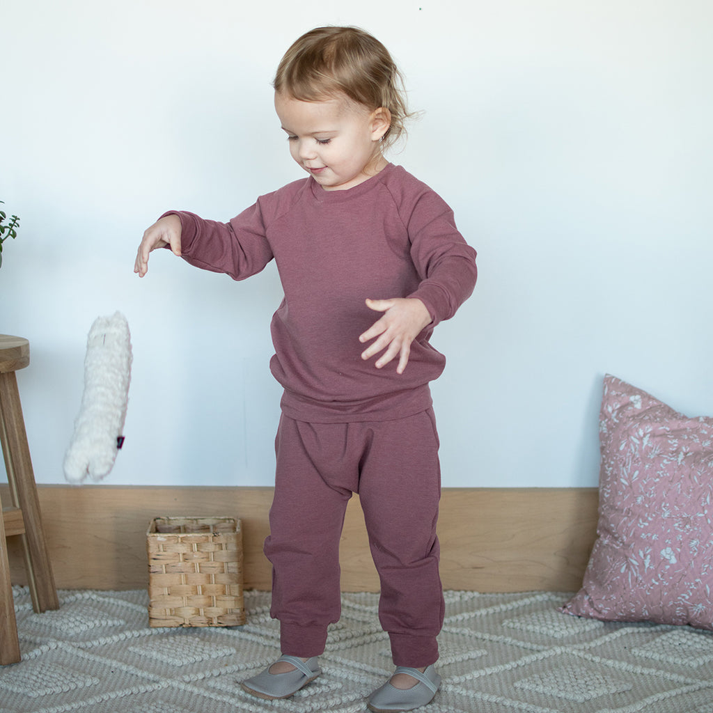 A toddler playing with toys, wearing a Berry pullover and harem pants.