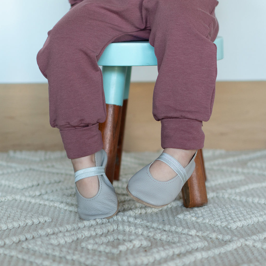 A toddler sitting on a stool, wearing harem pants in grow-with-me sizing. The colour is a warm berry tone with purple undertones.